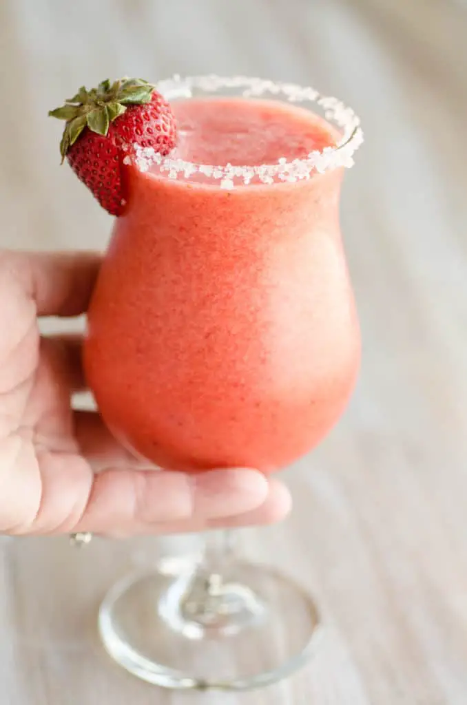 Fresh Virgin Strawberry Margaritas held in hand with a salted rim and strawberry garnish.