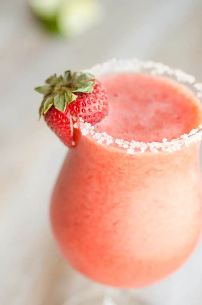 A close up of a fresh strawberry garnishing a glass of Fresh Virgin Strawberry Margaritas.