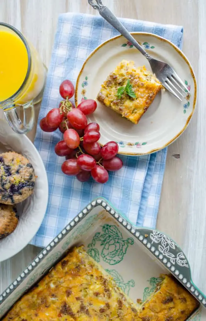 Make ahead breakfast Green Chile Breakfast Cubes or 'Chile Cubes' casserole sits on a wooden table top with grapes, orange juice, blueberry muffins and a casserole dish.