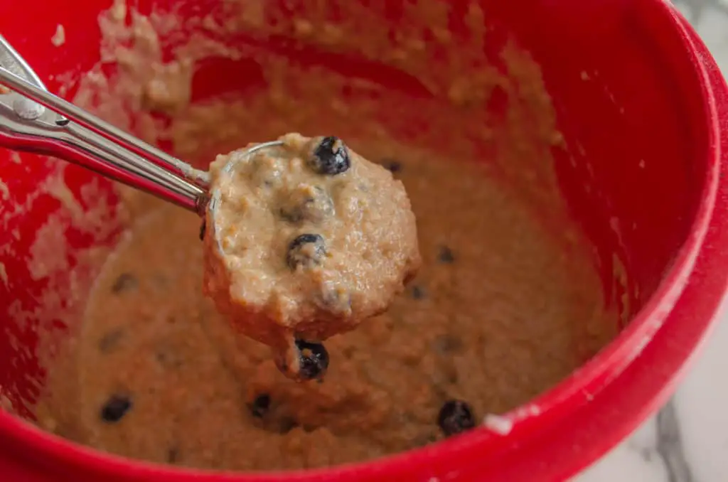 a closeup of batter in a scoop with blueberries in it for making Moist Whole Wheat Blueberry Swirl Muffins.