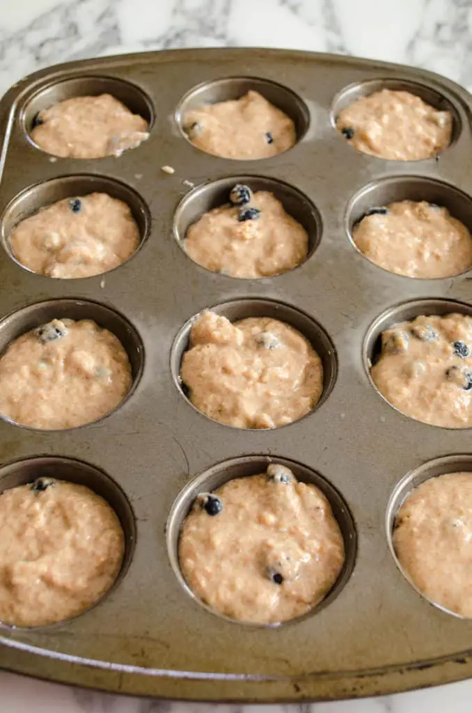 A muffin tin is filled with batter for Moist Whole Wheat Blueberry Swirl Muffins.