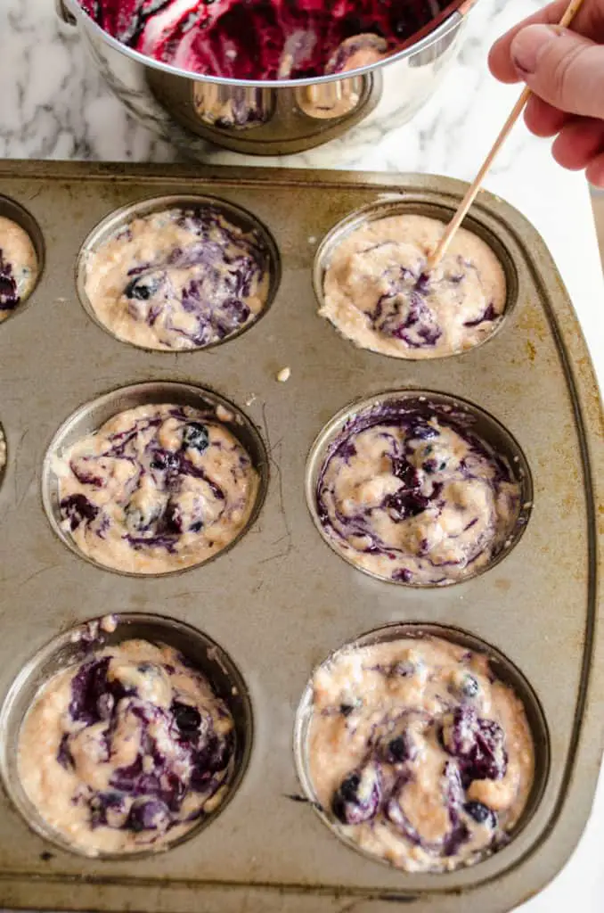 Fresh blueberry jam is swirled into Moist Whole Wheat Blueberry Swirl Muffins batter with a wooden skewer.