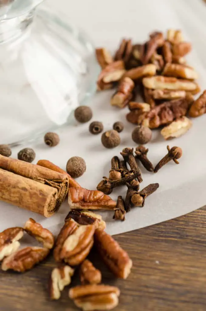 Allspice berries, whole cloves and a cinnamon stick are pictured with chopped pecans for Candied Spice Pecans- The Goldilocks Kitchen