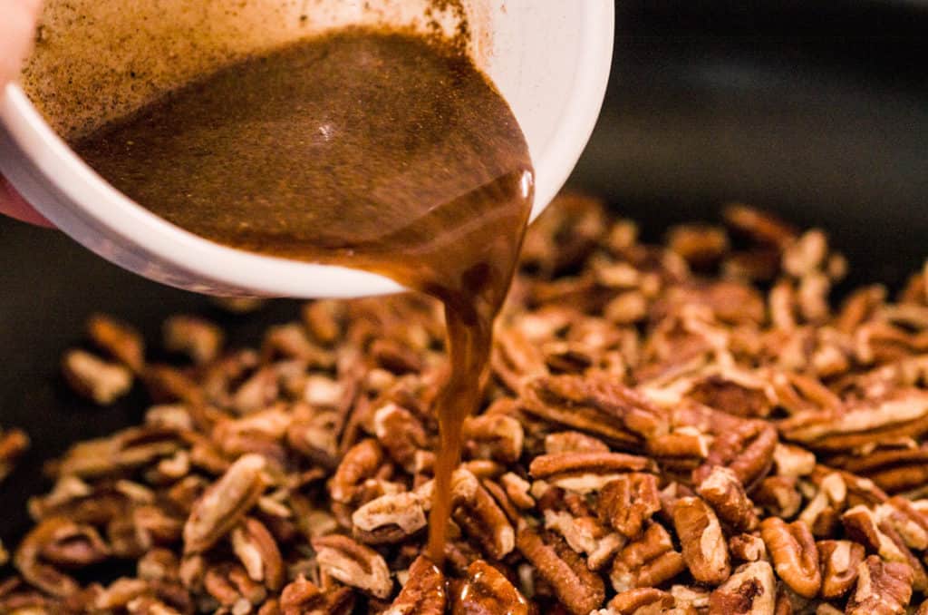 Sugar and spices mixed in water are poured out over a skillet of chopped pecans for Candied Spice Pecans- The Goldilocks Kitchen