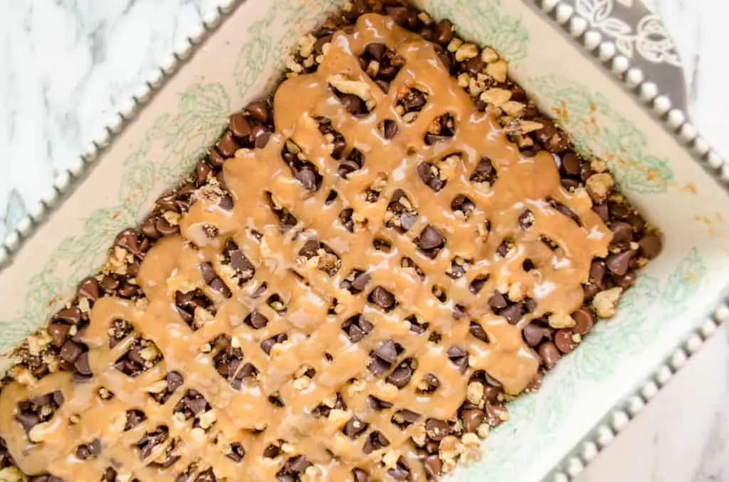 A close up of a decorative baking dish full of chocolate chips, nuts and caramel for Caramel Chocolate Oatmeal Chewies. -The Goldilocks Kitchen