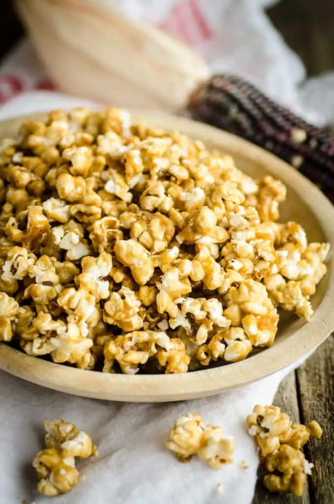A wooden bowl sits on a wooden table filled with Microwave Caramel Popcorn - The Goldilocks Kitchen