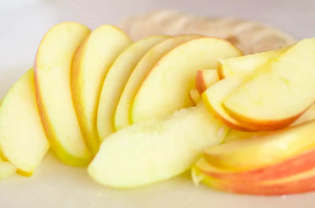 Sliced apples sit on a white cutting board ready for Chicken Apple Cheddar Salad. - The Goldilocks Kitchen