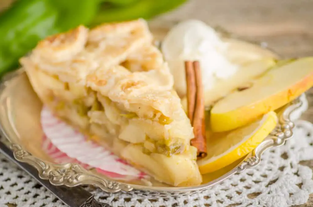 A slice of Green Chile Apple Pie sits on a silver decorative platter with slices of apple, lemon, a cinnamon stick and a scoop of ice cream - The Goldilocks Kitchen