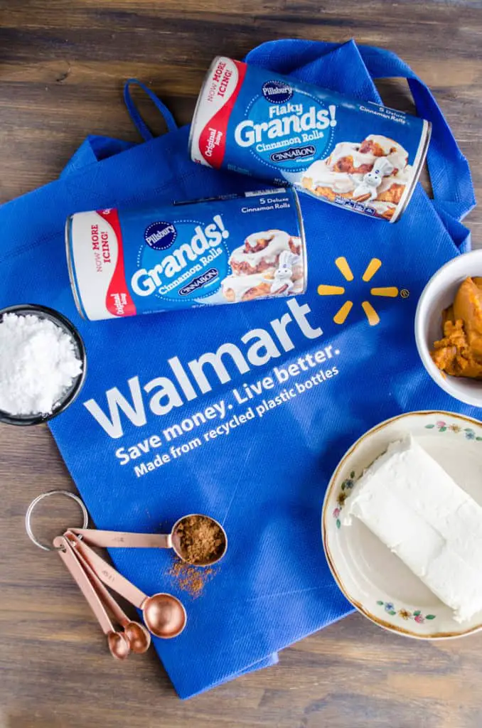 A blue Walmart bag is surrounded by cans of Pillsbury Grands! Cinnamon Rolls Original, pumpkin puree, a brick of cream cheese, powdered sugar and measuring spoons with spice in them to make a Pumpkin Pie Breakfast braid - The Goldilocks Kitchen