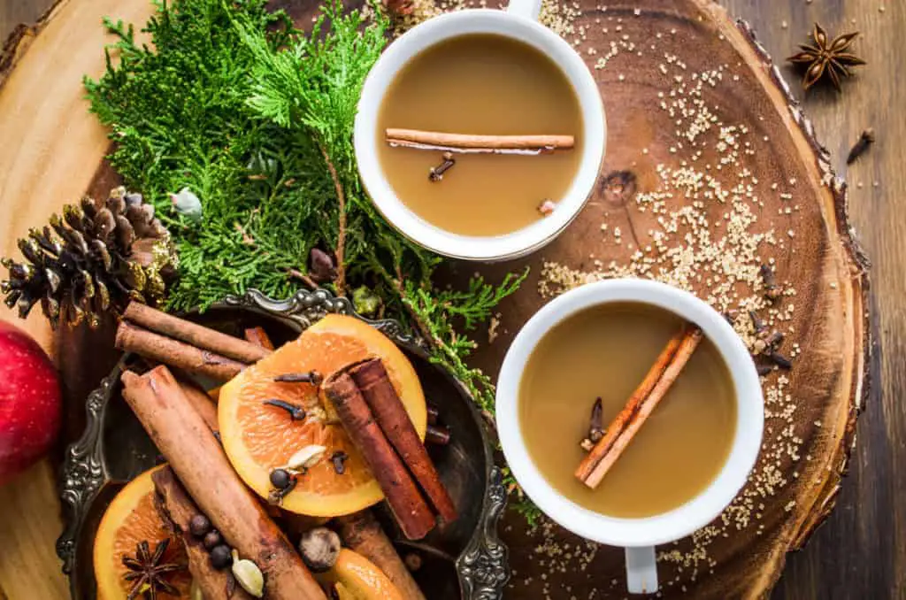Mulled Apple Cider a.k.a. Wassail in two white mugs with a cinnamon stick and cloves floating on top.