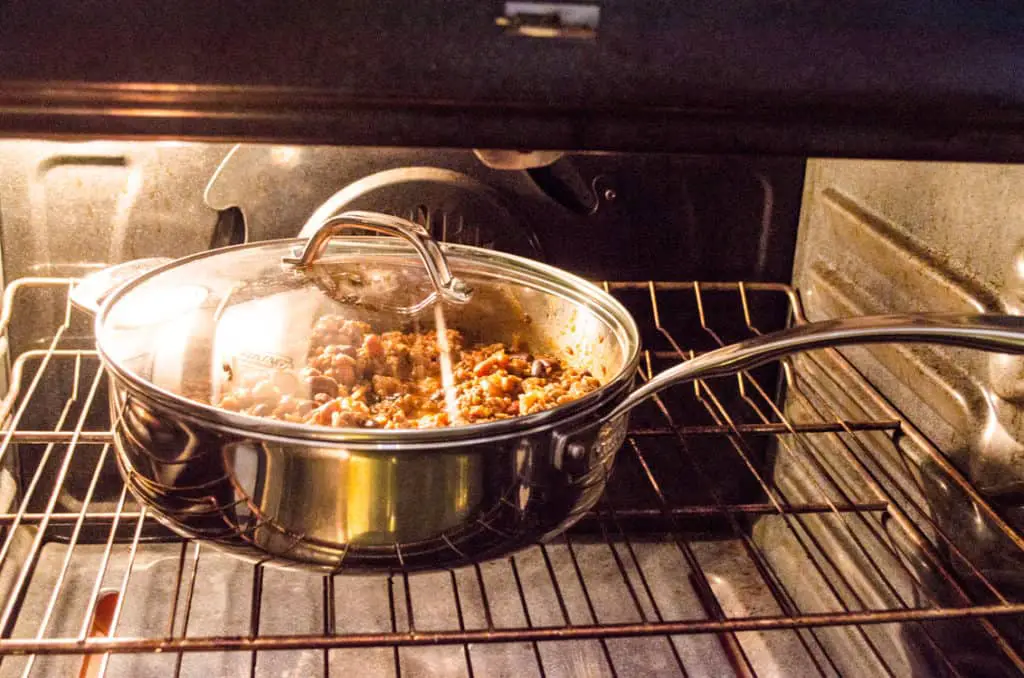 A stainless steel skillet full of The Best Dang Baked Beans is placed in an oven to bake. - The Goldilocks Kitchen