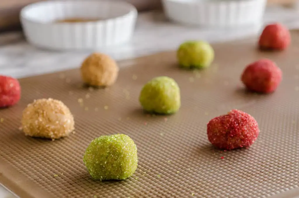 Cookie dough balls rolled in green, brown and red sugar crystals sit on a cookie sheet waiting to become Dove Peanut Butter Buttons cookies - The Goldilocks Kitchen