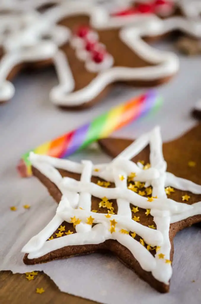 A closeup picture of a Easy Gingerbread Cookies star decorated with white frosting and edible golden glitter stars- The Goldilocks Kitchen