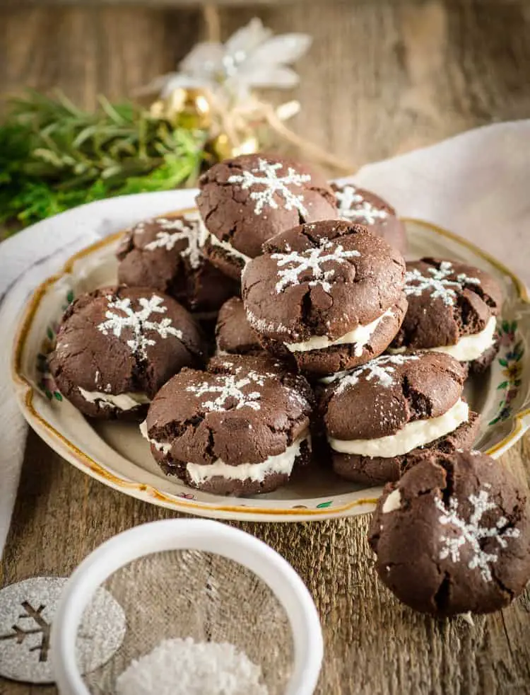 Homemade Oreo Cookies sit on a small plate on a wooden tabletop, decorated with powdered sugar stencils of snowflakes on top - The Goldilocks Kitchen