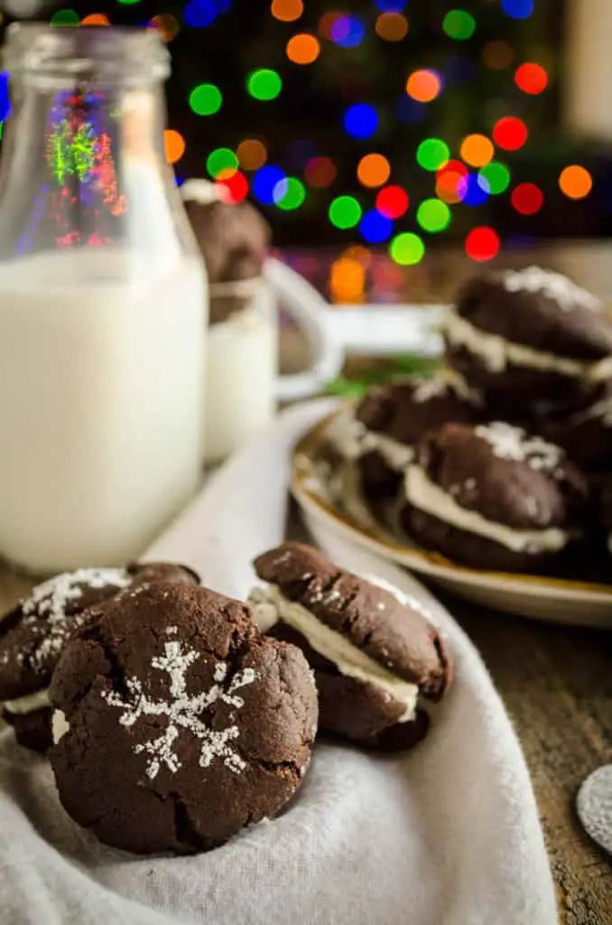 A closeup of Homemade Oreo Cookies with a jug of milk and Christmas lights in the background - The Goldilocks Kitchen