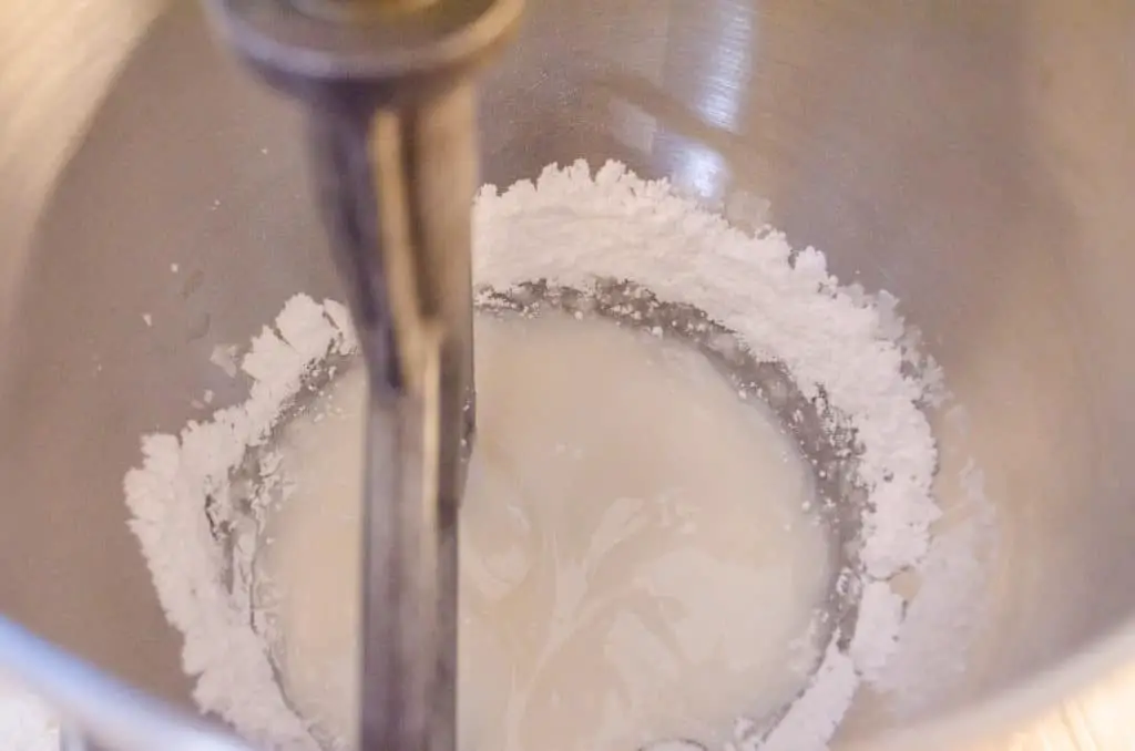 Powdered sugar is beaten into egg white and vanilla extract in a silver stand mixer bowl to make Royal Icing Gingerbread Frosting - The Goldilocks Kitchen