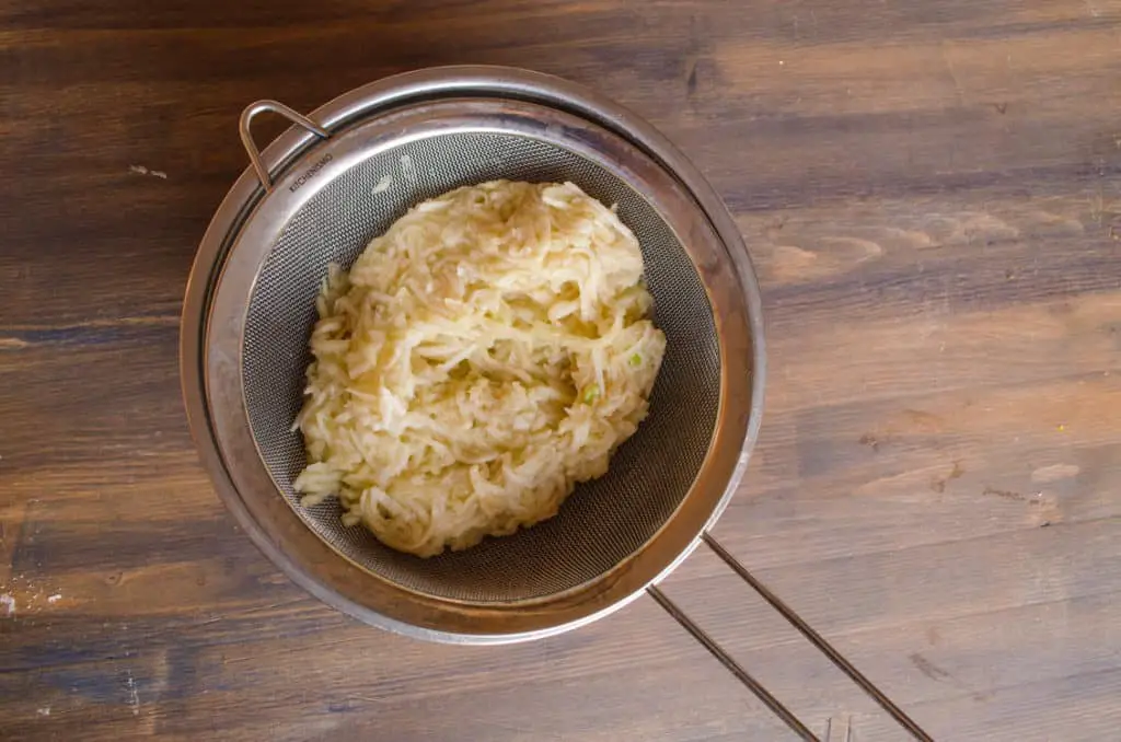 Shredded apple sits in a sieve over a bowl to allow excess liquid to drain to make Easy Apple Turnovers - The Goldilocks Kitchen