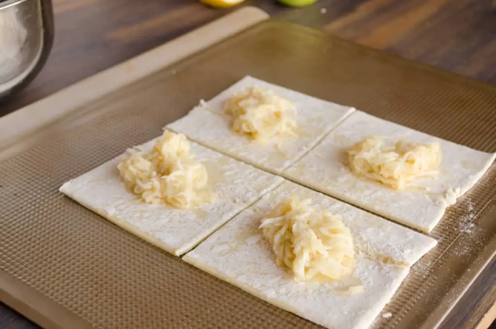 Squares of puff pastry with a small mound of shredded apple in the center are waiting to be folded into Easy Apple Turnovers - The Goldilocks Kitchen