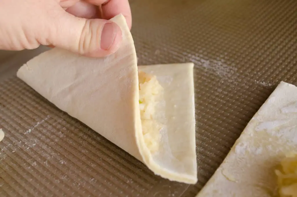 A square of puff pastry is being folded over shredded apple to form Easy Apple Turnovers - The Goldilocks Kitchen