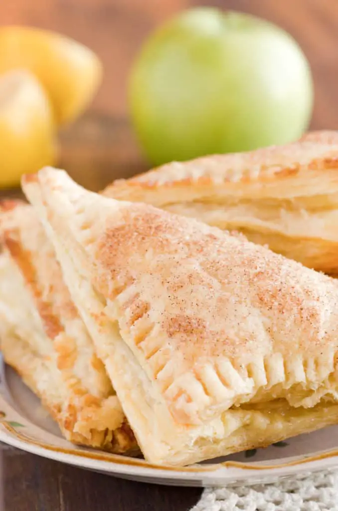A close up picture of three Easy Apple Turnovers on a small plate with an apple and lemons in the background - The Goldilocks Kitchen