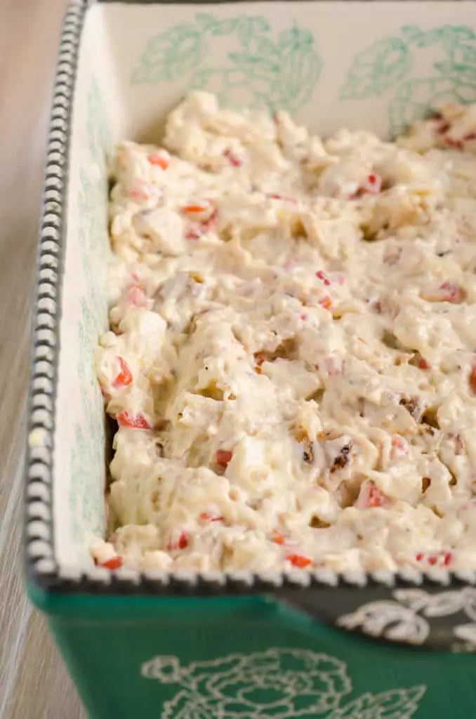 A green and white decorative casserole dish filled halfway with a mixture of creamy shredded chicken and pimiento peppers for a Creamy Chicken Biscuit Bake - The Goldilocks Kitchen
