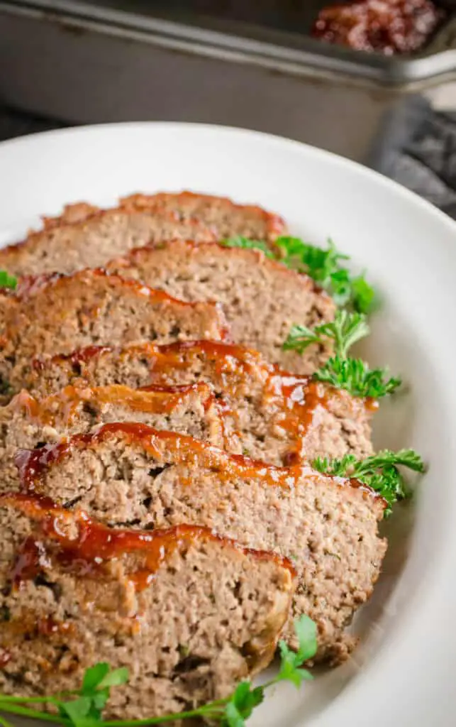 Meatloaf slices on a white ceramic serving platter garnished with sprigs of parsley - The Goldilocks Kitchen