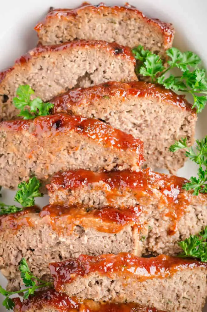 Glazed Meatloaf Slices sit in a white ceramic serving dish and are garnished with parsley - The Goldilocks Kitchen