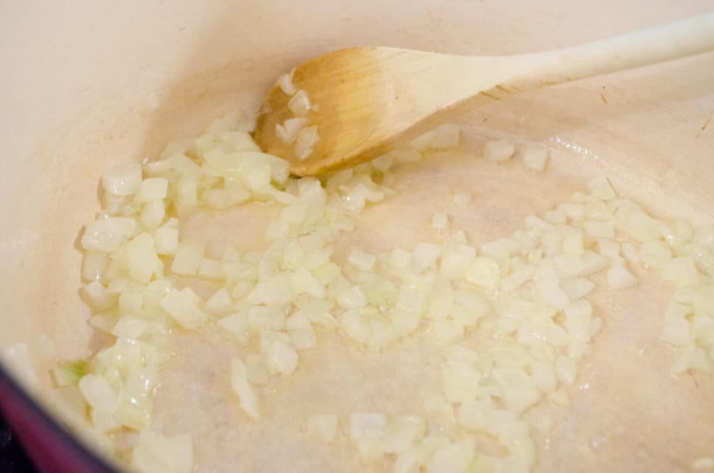 Diced onion cooking in a white enamel dutch oven for Cheesy Cauliflower Broccoli Bake - The Goldilocks Kitchen