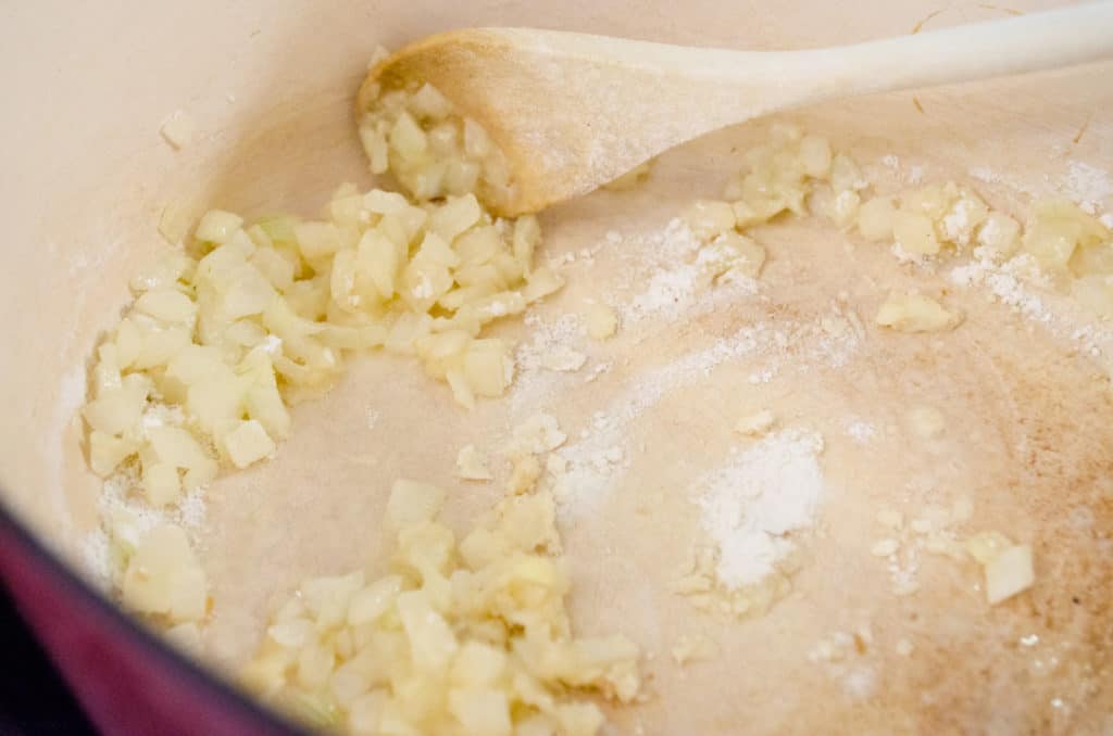 Flour is mixed into cooked diced onion for Cheesy Cauliflower Broccoli Bake - The Goldilocks Kitchen