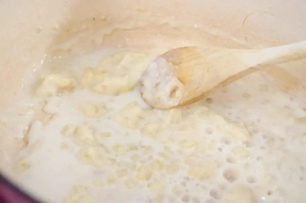 Milk is added to the onion and flour to make a white sauce for Cheesy Cauliflower Broccoli Bake - The Goldilocks Kitchen