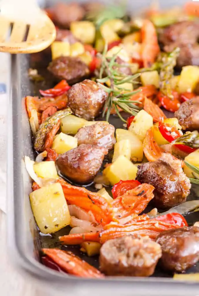 30 Minute Italian Sausage Sheet Pan Dinner close up pic in the sheet pan showing roasted carrots, potatoes, sausage pieces, red bell pepper and asparagus - The Goldilocks Kitchen