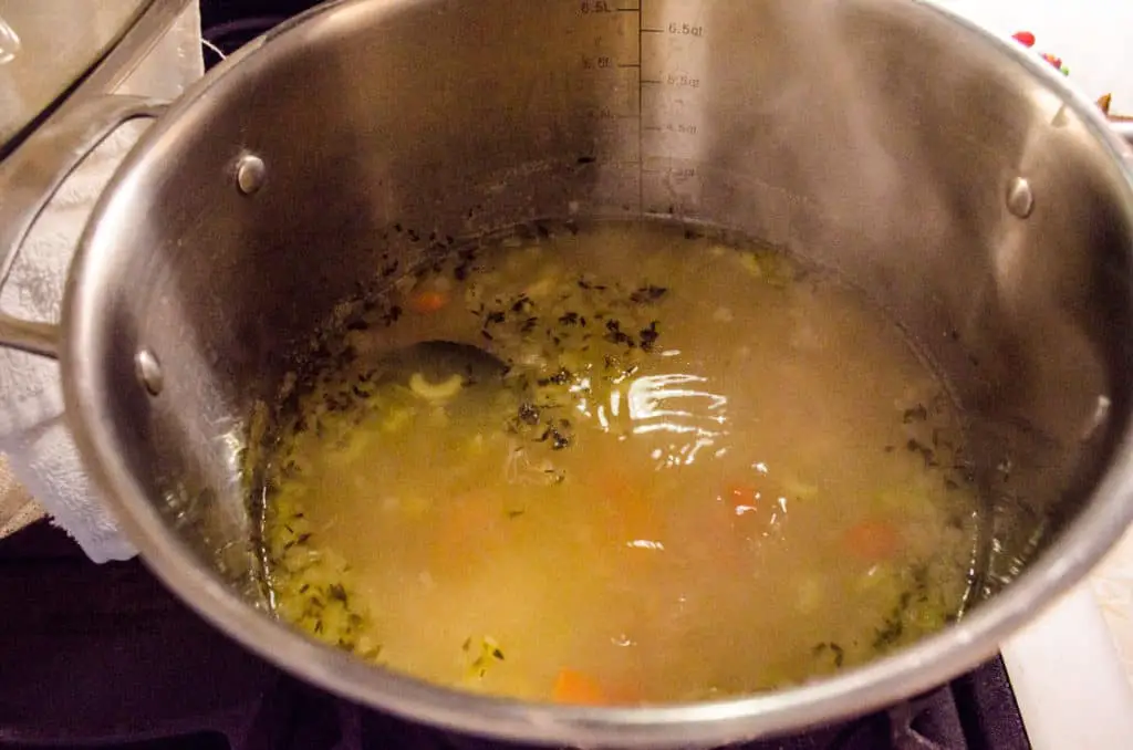 Broth, vegetables and herbs are simmered in a stainless steel pot to make Make Ahead Chicken Noodle Soup - The Goldilocks Kitchen