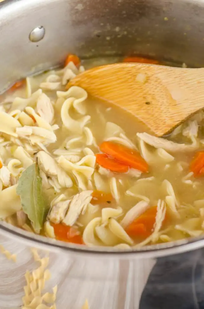 Make Ahead Chicken Noodle Soup in a stainless steel pot with carrots and a bay leaf - The Goldilocks Kitchen