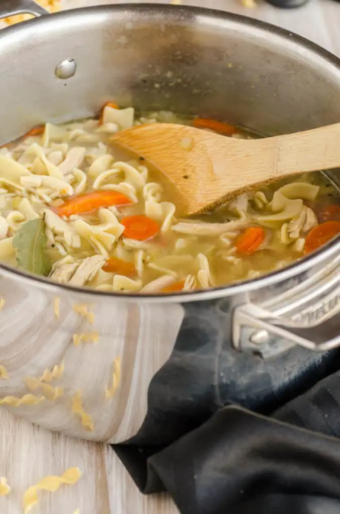 Make Ahead Chicken Noodle Soup in a pot with a large wooden spoon - The Goldilocks Kitchen