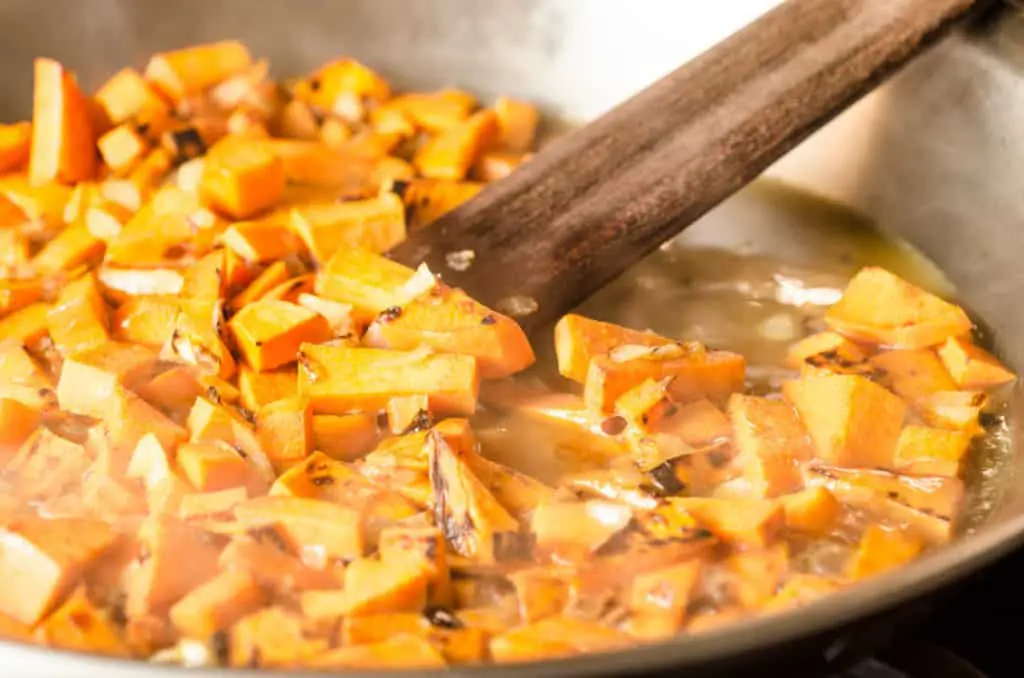 Diced sweet potato and onion is sauteed in a stainless steel skillet for Black Bean Sweet Potato Enchiladas - The Goldilocks Kitchen