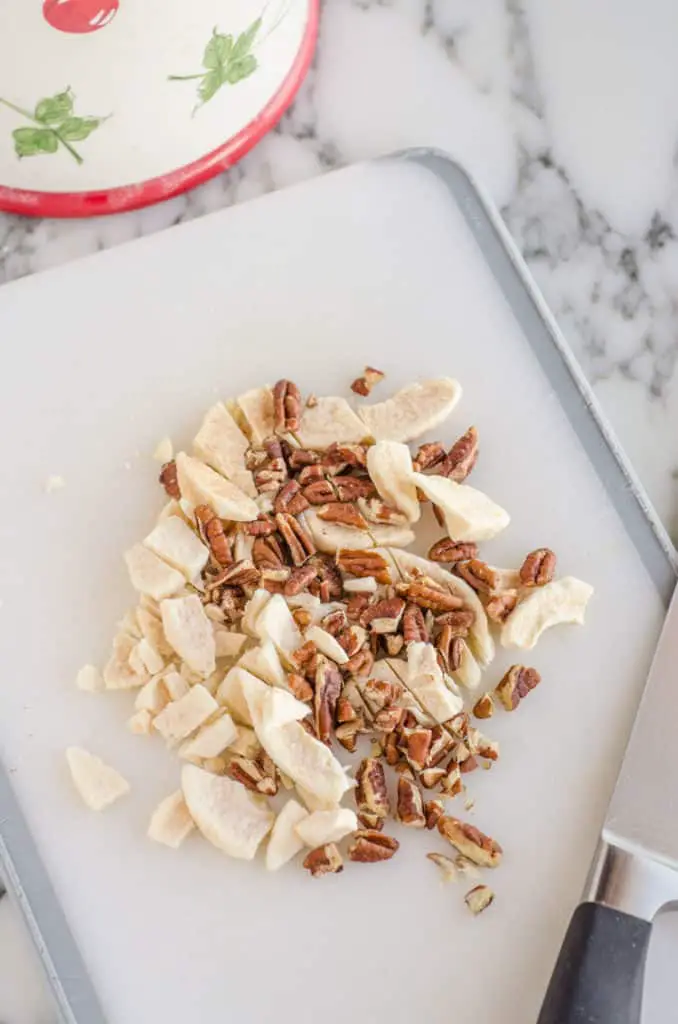 Pecans and dried apple slices are chopped on a white cutting board for Applesauce Picnic Cake - The Goldilocks Kitchen