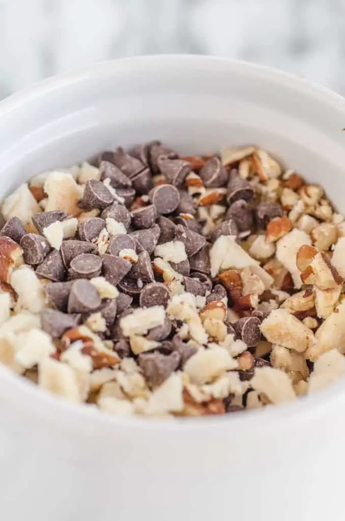 Mini-chocolate chips, diced pecans, and diced freeze dried apple slices mixed together in a white ceramic cup as a topping for Applesauce Picnic Cake - The Goldilocks Kitchen