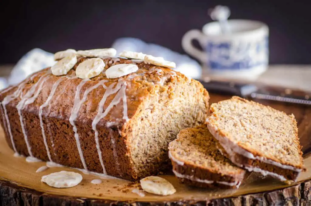 A Orange Spice Banana Bread loaf drizzled with glaze has a few slices sitting next to the loaf - The Goldilocks Kitchen