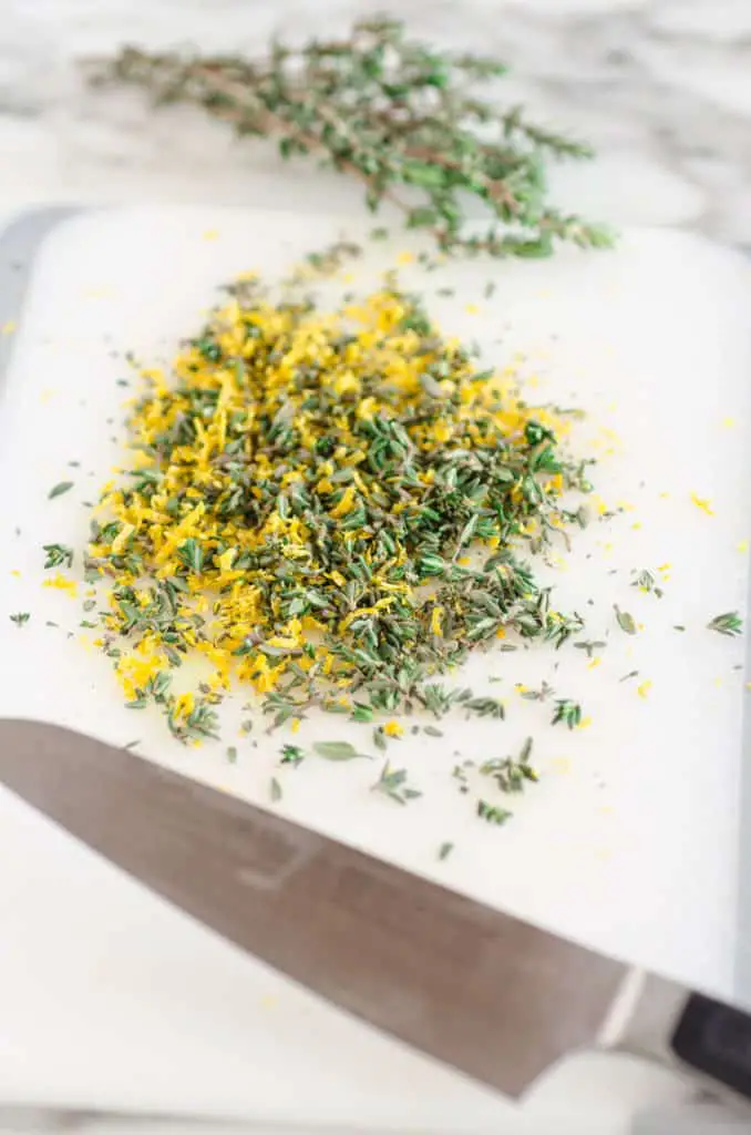 Freshly minced thyme leaves mixed with lemon zest on a white cutting board to make Whole Roasted Chicken and Sweet Potatoes - The Goldilocks Kitchen