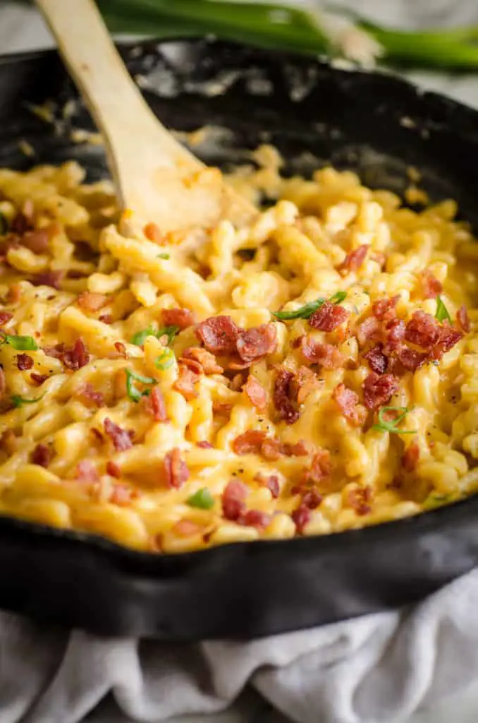 A close up picture of a black cast iron skillet filled with One-Skillet Bacon Mac and Cheese sprinkled with bacon and minced scallions on top - The Goldilocks Kitchen