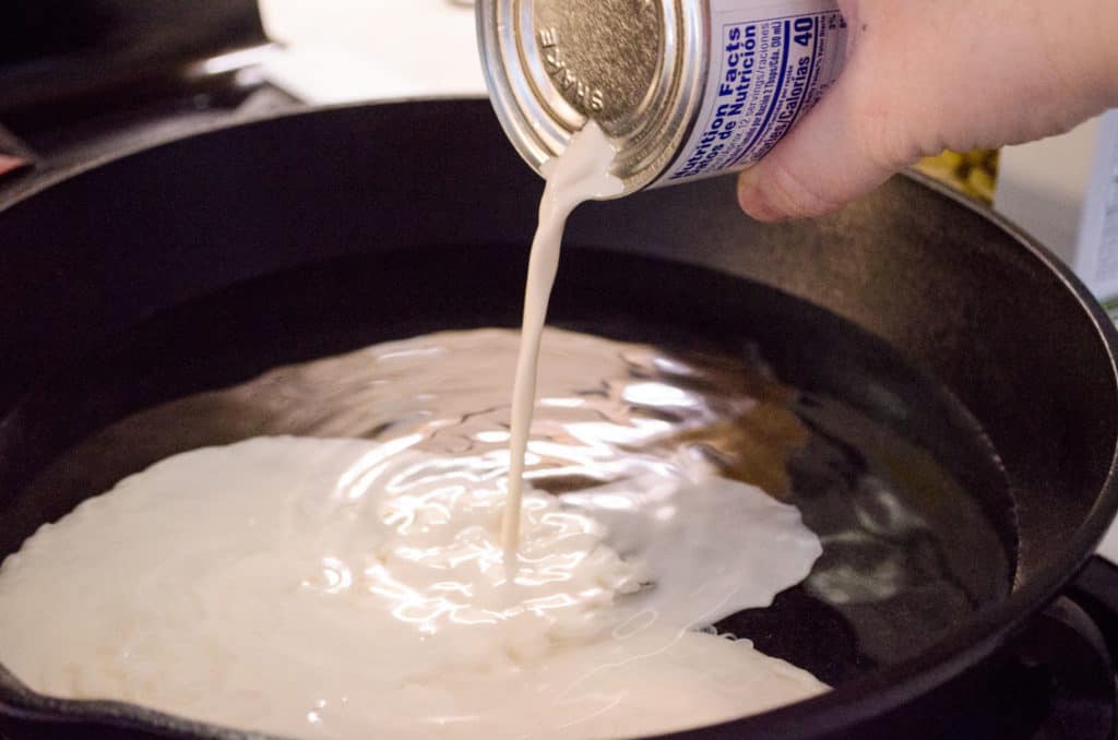 Evaporated milk is poured into a cast-iron skillet with water in it to make One-Skillet Bacon Mac and Cheese - The Goldilocks Kitchen