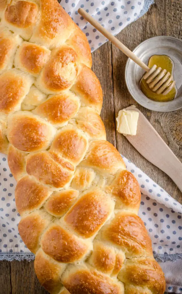 Looking down on a golden Braided Challah Bread loaf on a wooden table - The Goldilocks Kitchen