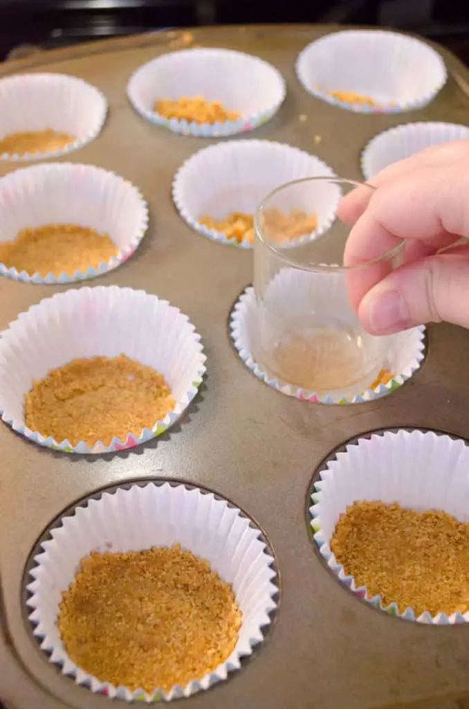 Graham cracker crust is pressed into the bottoms of cupcake liners placed into a muffin tin to make Strawberry Mini-Cheesecakes - The Goldilocks Kitchen