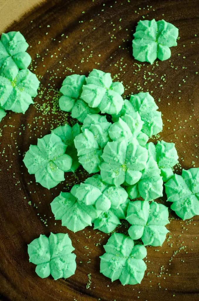 Green clover shaped St. Patricks Day Cream Cheese Spritz Cookies sit on a wooden platter - The Goldilocks Kitchen