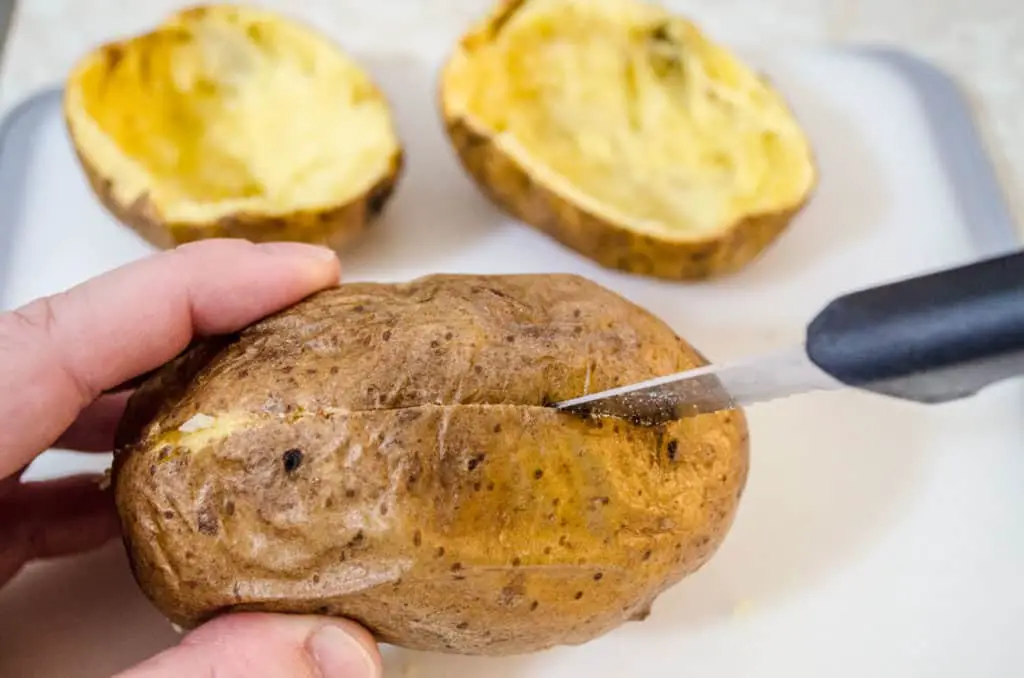 Holding a baked potato sideways to slice it in half for Make Ahead Twice Baked Potatoes - The Goldilocks Kitchen
