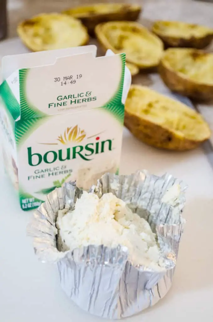 A chunk of boursin cheese sits in it's foil wrapper in front of the packaging box with potato shells in the background for making Make Ahead Twice Baked Potatoes - The Goldilocks Kitchen