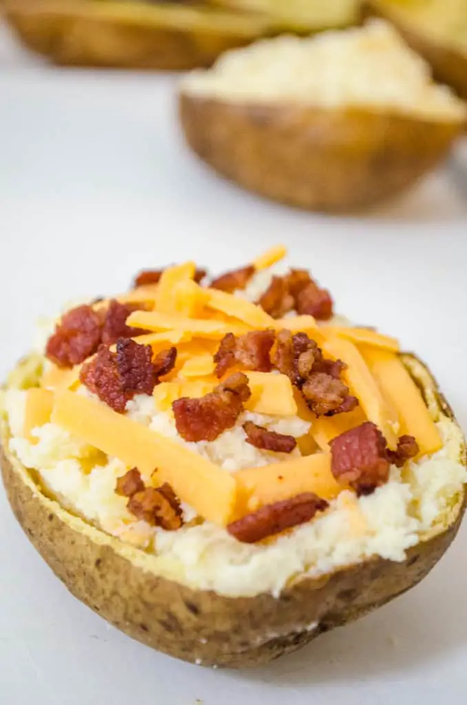 A close picture of a potato skin filled with potato filling, topped with shredded cheddar and bacon for Make Ahead Twice Baked Potatoes - The Goldilocks Kitchen