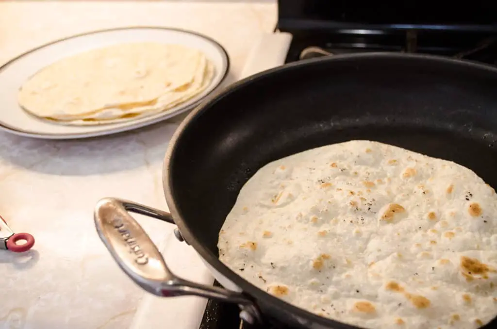Fresh flour tortillas are cooked on the stovetop in a large non-stick skillet for Grilled Chicken Tacos with Green Chile Cream Sauce - The Goldilocks Kitchen