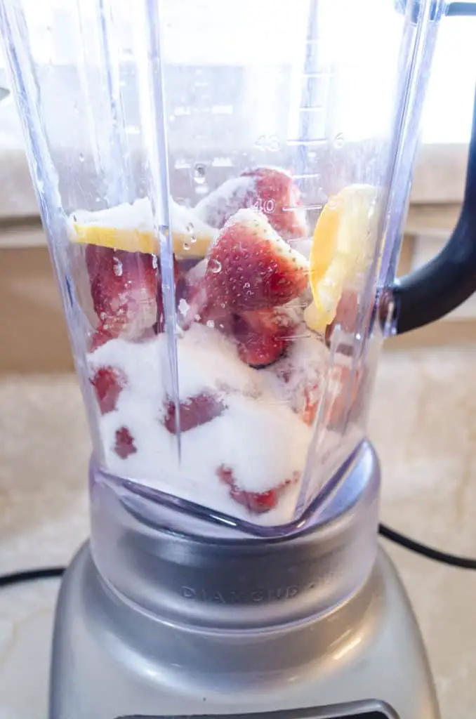 A blender is filled with strawberries, lemon slices and sugar for Fresh Sparkling Strawberry Lemonade - The Goldilocks Kitchen