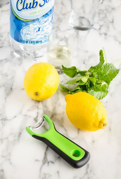 Two lemons, a bottle of club soda, simple syrup, an empty glass, fresh mint and an OXO Citrus Prep Peeler are all you need to make a fresh Lemonade Sparkler - The Goldilocks Kitchen